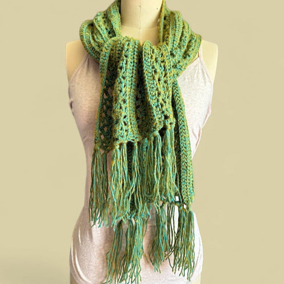 Moss Green crocheted lace scarf with fringe on a mannequin against a beige background