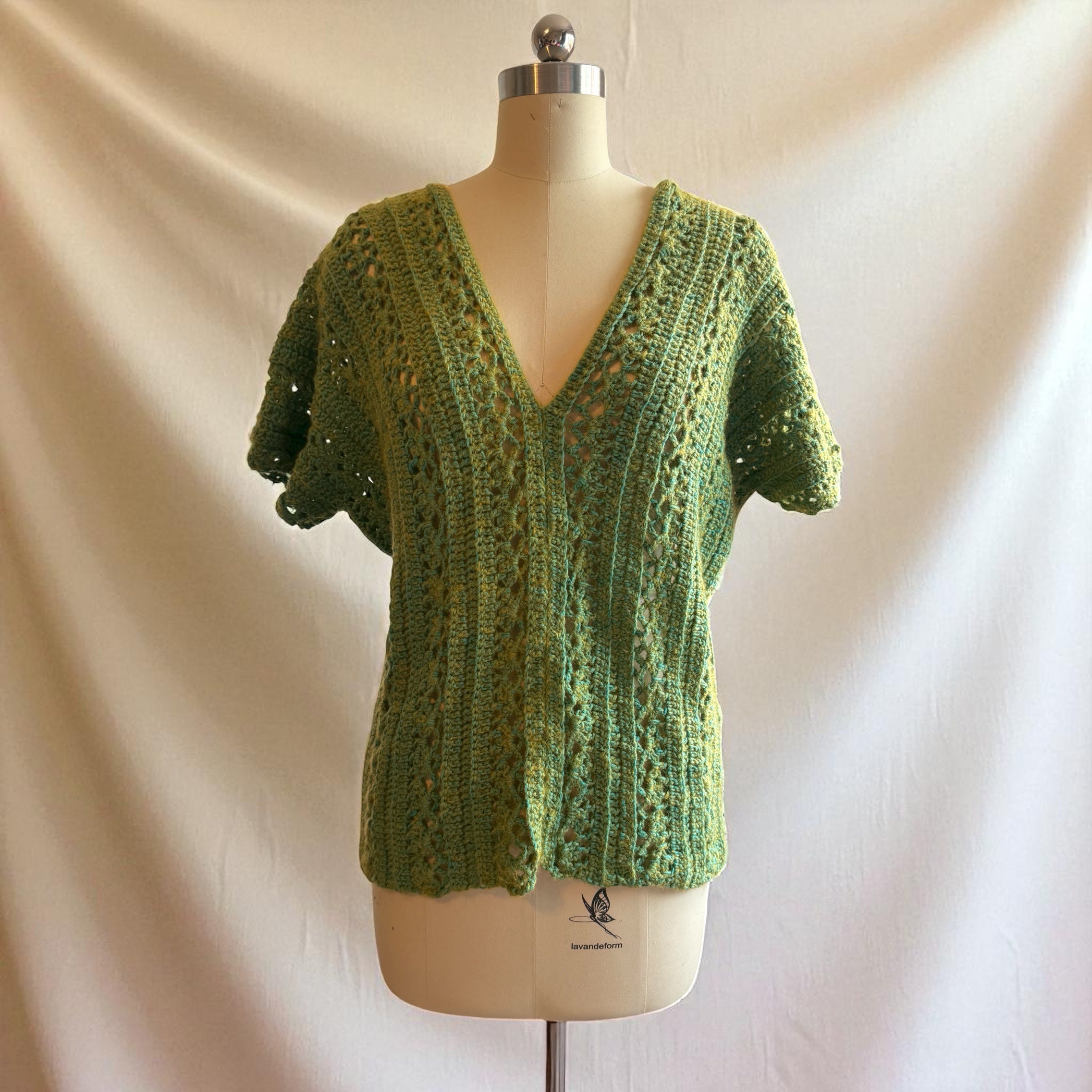 Moss Green crocheted top on a mannequin against a beige background